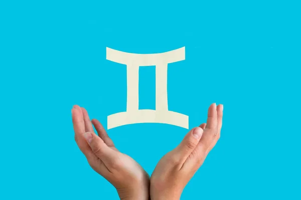 Gemini astrological sign hanging over female hands on blue background, horoscope forecast concept