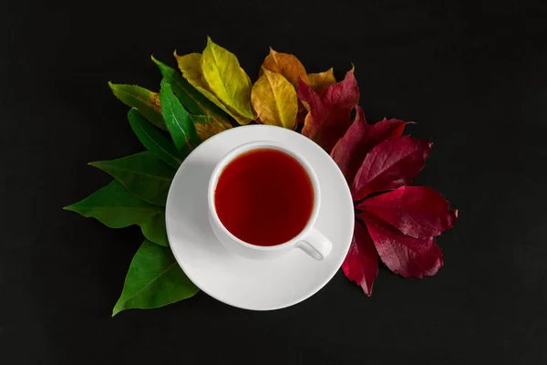 top view fall wallpaper with cup hot drink in a white cup and bouquet of autumn multicolored leaves on a black table background