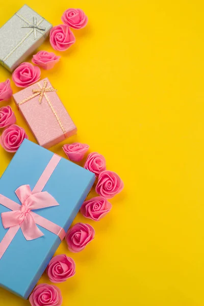 gift boxes and pink roses flat lay on a vibrant yellow background with free space for text
