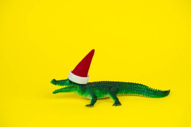 Komik yeşil timsah oyuncağı. Küçük Noel Baba şapkalı, parlak sarı arka planda.