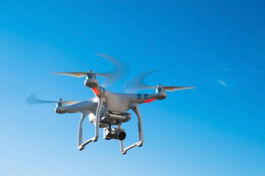 Mavi gökyüzüne karşı kameralı uçan bir dron.