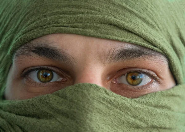 close up of the green eyes of a man whose face is covered with a blue bandage