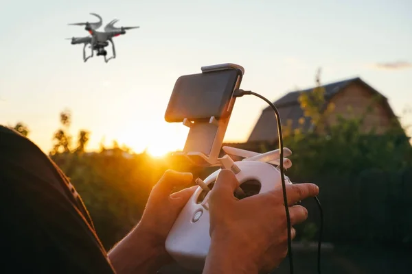 close up of a man\'s hand with a joystick controlling a drone with a smartphone against the background of the sunset sky