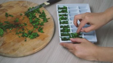 Buz yağı küpleri yapmak ikinci adım, kadın ellerini kapat dilimlenmiş yeşillikleri buz kalıbına dök.