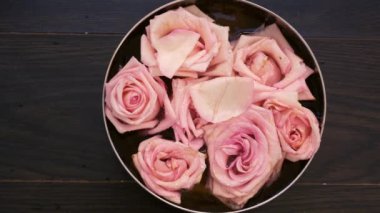 Su, pembe güller ve güllerle dolu bir kase üst kattan aşağı düşüyor ahşap arka plan, el ve çivi kaplama konsepti.