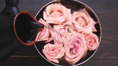 Bulanık odaklı üst görüş suyu, ahşap arka planda yumuşak pembe güller, spa ve kişisel bakım konsepti olan bir kaseye dökülür.