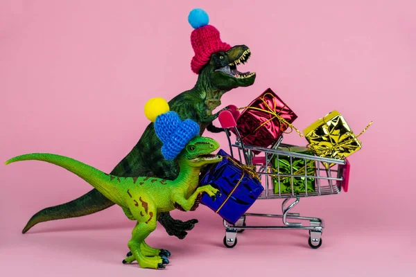 現在の箱でいっぱいのショッピングトロリー付きのニット帽の2つのかわいい恐竜 販売コンセプト — ストック写真