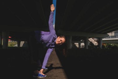 Köprünün altında egzersiz yapan genç bir kadın, karanlık, karamsar bir fotoğraf, aktif yaşam tarzı konsepti.