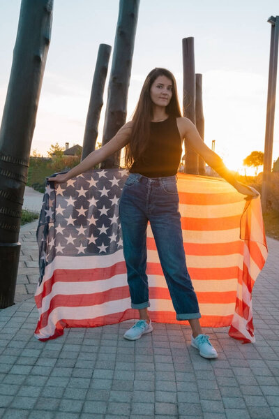 beautiful young woman with American flag in the park at the sunset