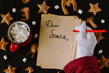 En üstteki düz görünüm, yıldız şeklinde zencefilli kurabiyeler ve mektuplar mutlu noeller ve yazılı eski kağıtlar sevgili Noel Baba ve siyah arka planda beyaz eldivenler.