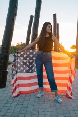Gün batımında parkta Amerikan bayrağı taşıyan güzel genç bir kadın.