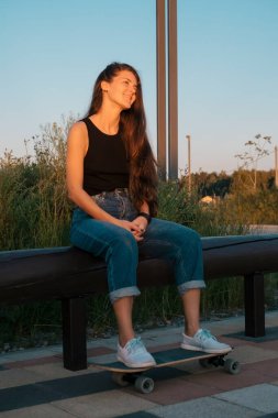 Parktaki bankta oturan kaykaylı güzel genç bir kadın.