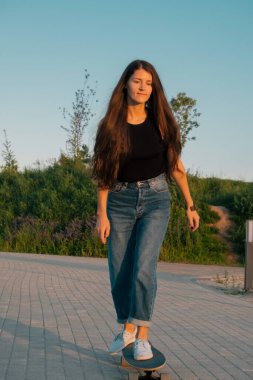 Genç esmer kadın yazın parkta kaykaya biniyor.