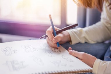 Kadın özgür-el sanat kalem ve kurşun kalem tarafından beyaz kağıt sıcak ışık yumuşak ses tonuyla penceresinden çizim gerçekleştirir.