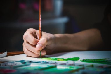 Genç kadın elindeki küçük resim fırçası lamba ışığı altında karanlık odada beyaz kağıt gemide suluboya boya kullanarak odak kapatın.