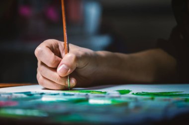 Genç kadın elindeki küçük resim fırçası lamba ışığı altında karanlık odada beyaz kağıt gemide suluboya boya kullanarak odak kapatın.