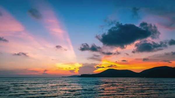 Panorama scene of colorful sunset sky at beach with silhouette mountain.