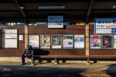 Ryoanji istasyonunda bir sonraki tren bekleyen bankta oturan turist
