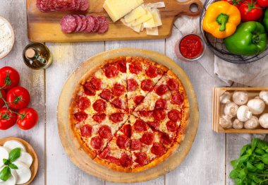 Ahşap tahta ve masa üzerinde taze pişmiş pepperoni pizza, renkli malzemelerle, havai üst görünümü