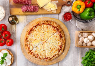 Ahşap tahta ve masa üzerinde taze pişmiş bütün peynirpizza, renkli malzemelerle, havai üst görünümü