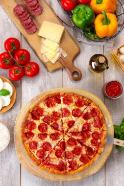 Ahşap tahta ve masa üzerinde taze pişmiş pepperoni pizza, renkli malzemelerle, dikey havai üst görünümü
