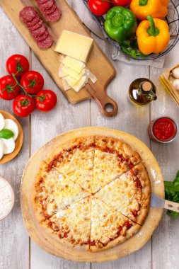 Ahşap tahta ve masa üzerinde taze pişmiş peynir pizza, renkli malzemelerle, dikey havai üst görünümü