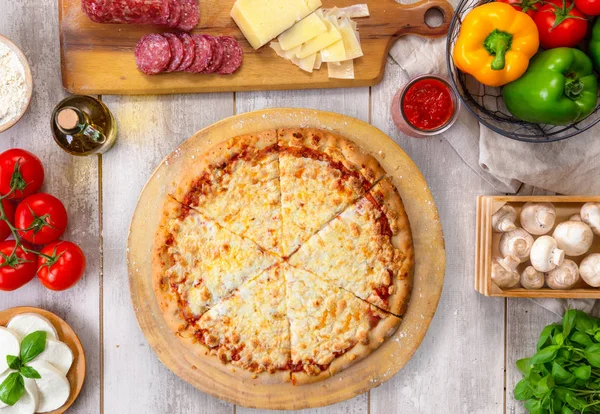 Ahşap tahta ve masa üzerinde taze pişmiş bütün peynirpizza, renkli malzemelerle, havai üst görünümü