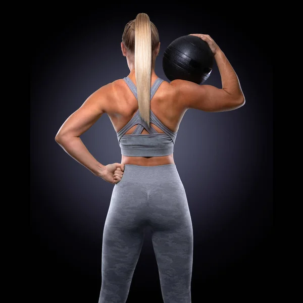 Strong confident power stance, female trainer with medicine ball, toned buttocks, upper body workout, majestic pose from behind, backside, back muscles, butt, arms