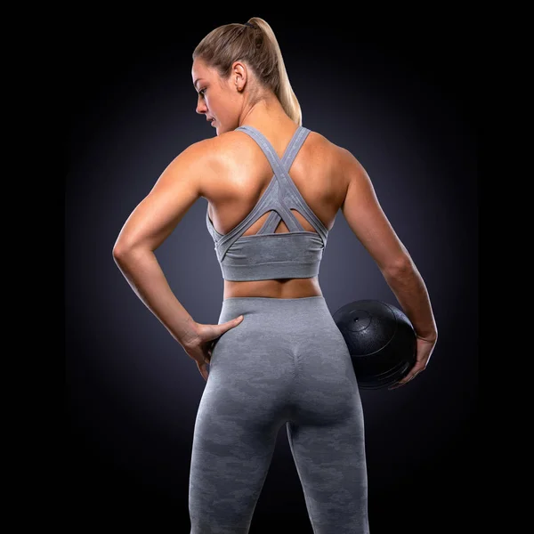 Strong confident power stance, female trainer with medicine ball, toned buttocks, upper body workout, majestic pose from behind, backside, back muscles, butt, arms