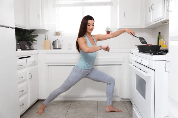 Woman multitasking while cooking, preparing meal, exercising yoga and stretching in the kitchen to save time