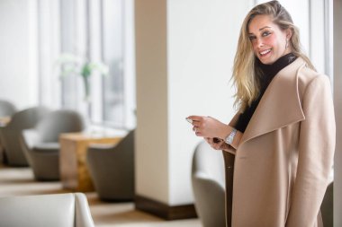 Göz kamaştırıcı lüks moda ceketli, cep telefonlu, modern ofis içinde gülümseyen güzel, neşeli bir iş kadını.