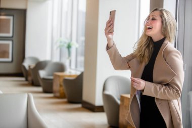 Lüks ofis süitinde şık, modern iş kadını girişimci. Gülümsüyor ve akıllı telefondan görüntülü sohbet ediyor., 