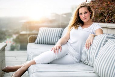 Güzel bir kadın gün batımında teras güvertesindeki kanepesinde dinleniyor. Lüks apartman dairesi.