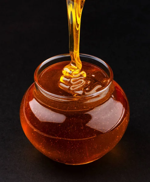 Pote de derramamento de mel no fundo preto — Fotografia de Stock