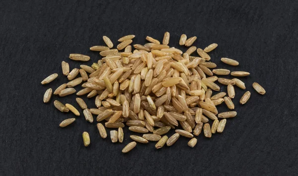 Brown rice groats on black background — Stock Photo, Image