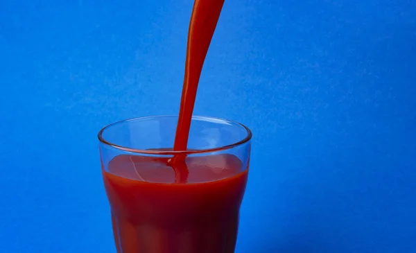 Jus de tomate versé dans le verre, isolé sur fond bleu, avec espace de copie — Photo