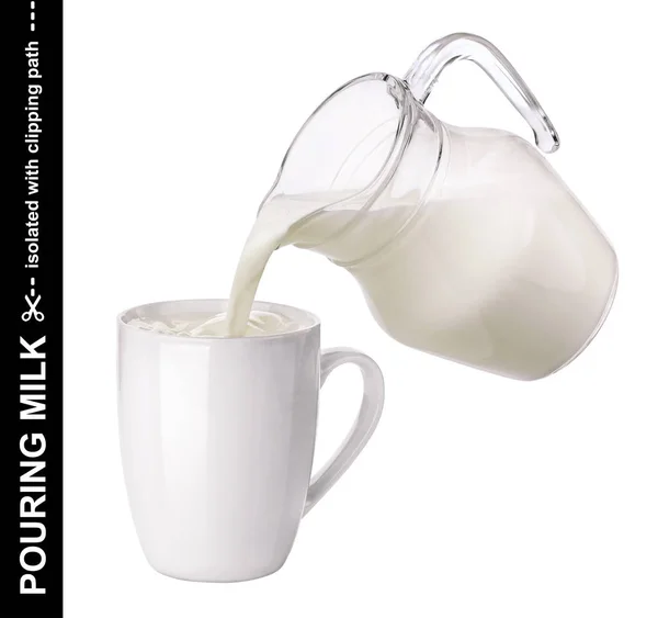 Gieten van melk van glazen kruik in beker geïsoleerd op witte achtergrond — Stockfoto