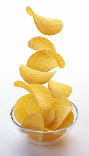 Картофельные чипсы, падающие в стеклянную чашу на белом фоне — стоковое фото