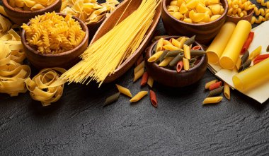 Siyah zemin üzerinde farklı makarna türleri metin için kopyalama alanı, italyan gıda malzemeleri konsepti, koyu taş masa üzerinde kurumuş makarna koleksiyonu üst görünümü