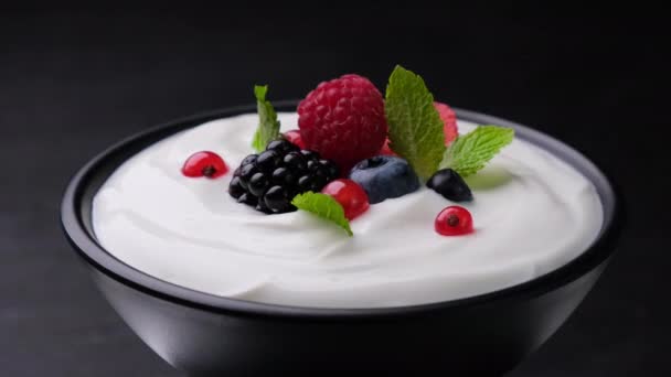 Bowl of yogurt with wild berries on black background — Stock Video