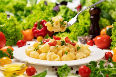 Bir tabak İtalyan makarnası, çatallı pipo domates ve fesleğen yapraklı.