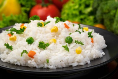 Pişmiş pirinç lapası, siyah tabakta bitki ve sebzelerle servis edilir.