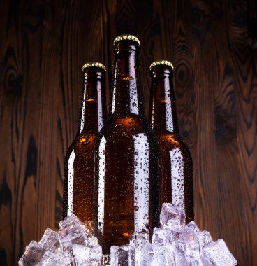 Su damlalı soğuk bira, siyah ahşap arka planda buzlu bira şişeleri.