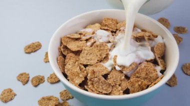 Kepekli gevreklerle dolu kaseye süt dökülüyor, sağlıklı kahvaltılık gevrek.