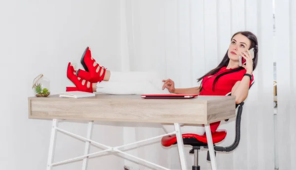 girl is sitting at the office feet on the table, talking on the phone