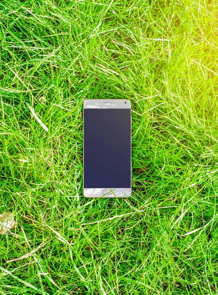 Mobile phone lies on the green grass background