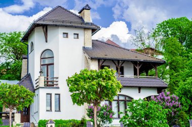 Ev Akdeniz tarzı, yeşil ağaçlar ve önünde leylak çalılar