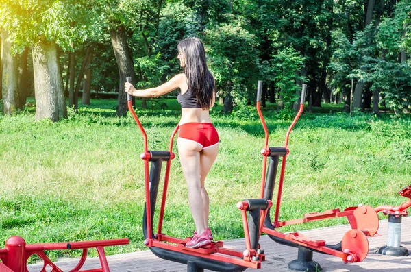 Brunette girl in red shorts is engaged in a street sports simulator in the park