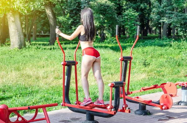 Brunette girl in red shorts is engaged in a street sports simulator in the park