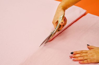 Kadın eli pembe kumaş makas ile keser..